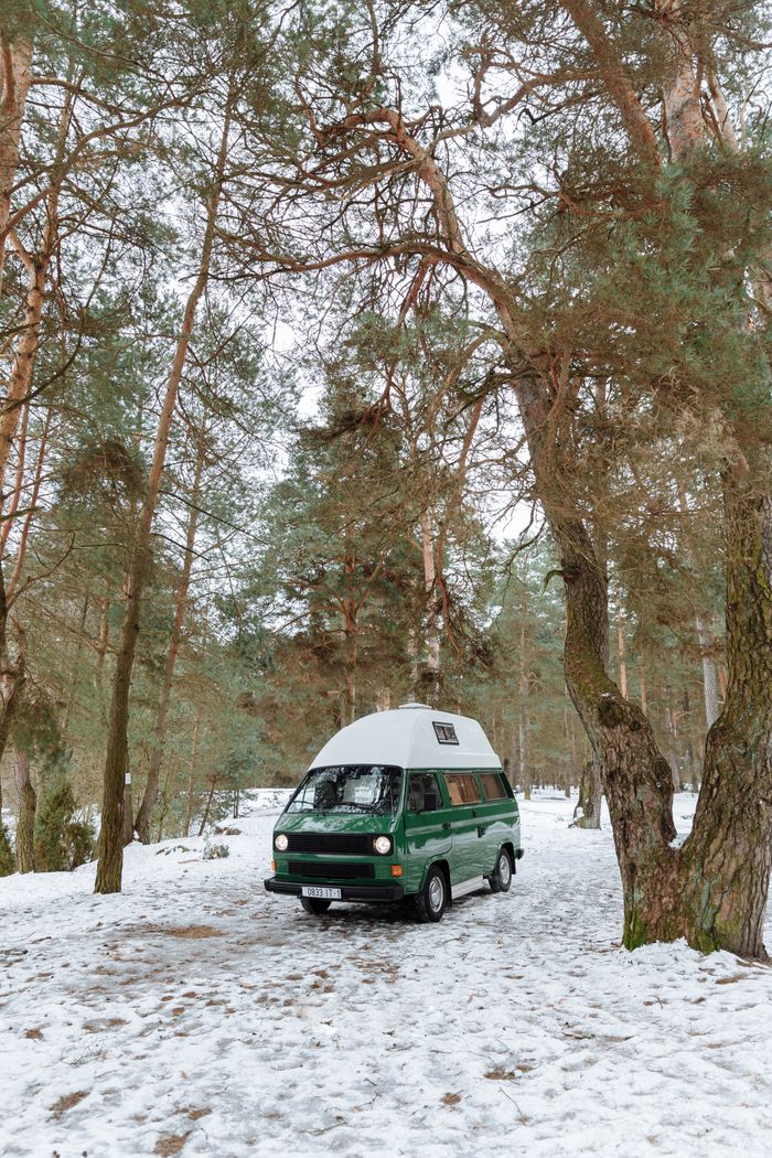Green vintage campervan parked in a serene snowy forest during winter.